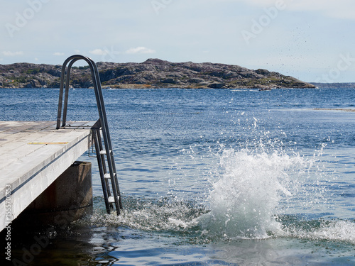 A young boy jumping from a pier in to the water a clear sunny summer day