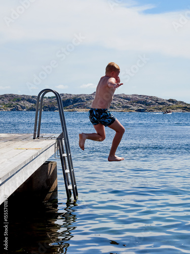 A young boy jumping from a pier in to the water a clear sunny summer day