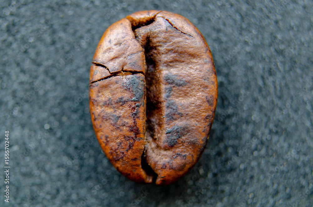 Naklejka premium A crisp and detailed closeup shot of a roasted coffee bean displaying its natural texture and deep brown color on a dark gray surface