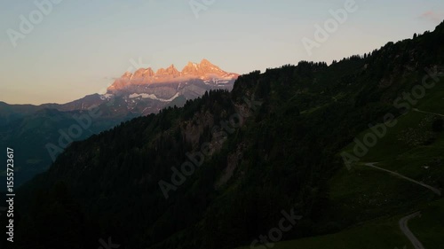 Beautiful Sunset drone flight in the Swiss Alps. Drone pans behind the tree line looking at the pink sunset on the peaks of the Dents du Midi in the Val d'Illiez of Canton Valais in Switzerland.