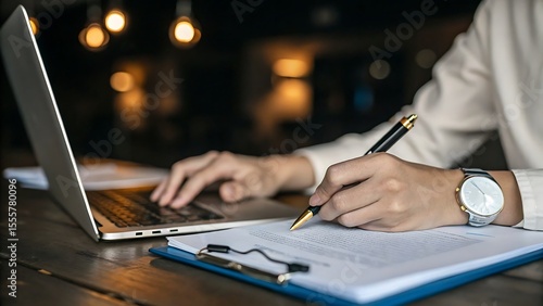 Person writing on document with pen next to laptop and wearing a wristwatch