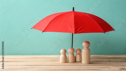 Red umbrella protecting wooden family figures on a wooden surface against teal background protection