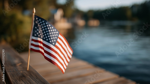 Fototapeta Naklejka Na Ścianę i Meble -  American flag on wooden pier by tranquil lake at golden hour