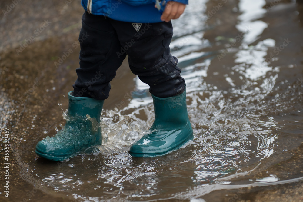 child splashing in puddle with green rubber boots during rainy day playtime wearing waterproof clothing on wet street joyful outdoor kids activity in rain shallow water reflections fun childhood momen child splashing in puddle with green rubber boots during rainy day playtime wearing waterproof clothing on wet street joyful outdoor kids activity in rain shallow water reflections fun childhood momen