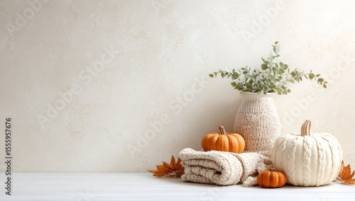 Fototapeta Naklejka Na Ścianę i Meble -  Autumnal scene with pumpkins, a knit blanket, eucalyptus in a textured vase, and fall leaves against a beige backdrop
