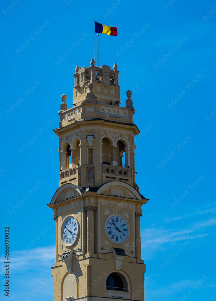 Obraz premium Oradea City Hall Tower in Union Square. Clock tower with the Romanian flag waving in the wind on a blue sky background
