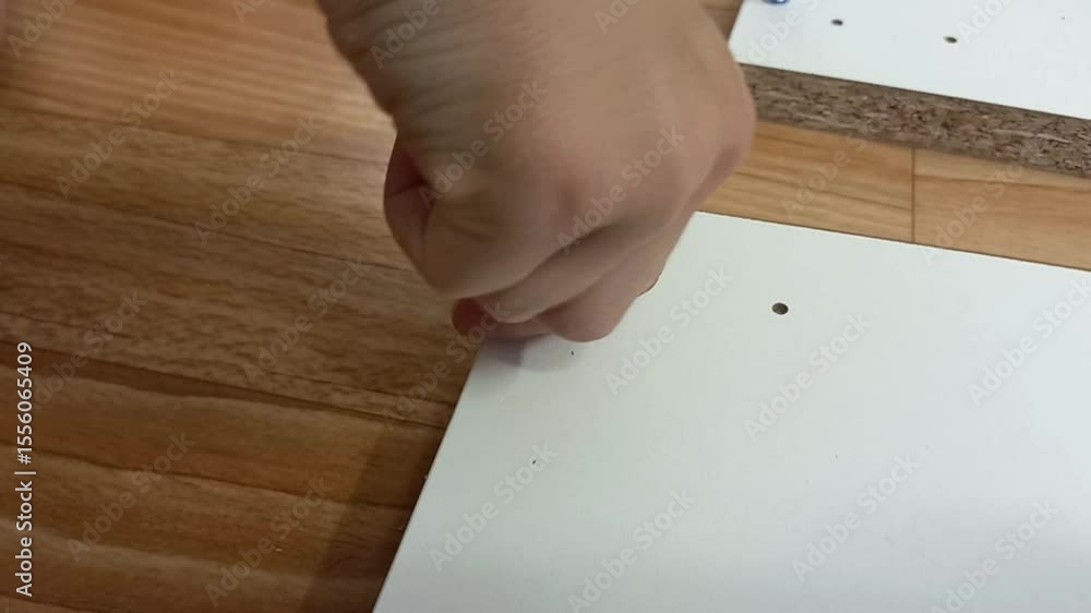 Hand securing a screw into a white board on wooden surface Hand securing a screw into a white board on wooden surface