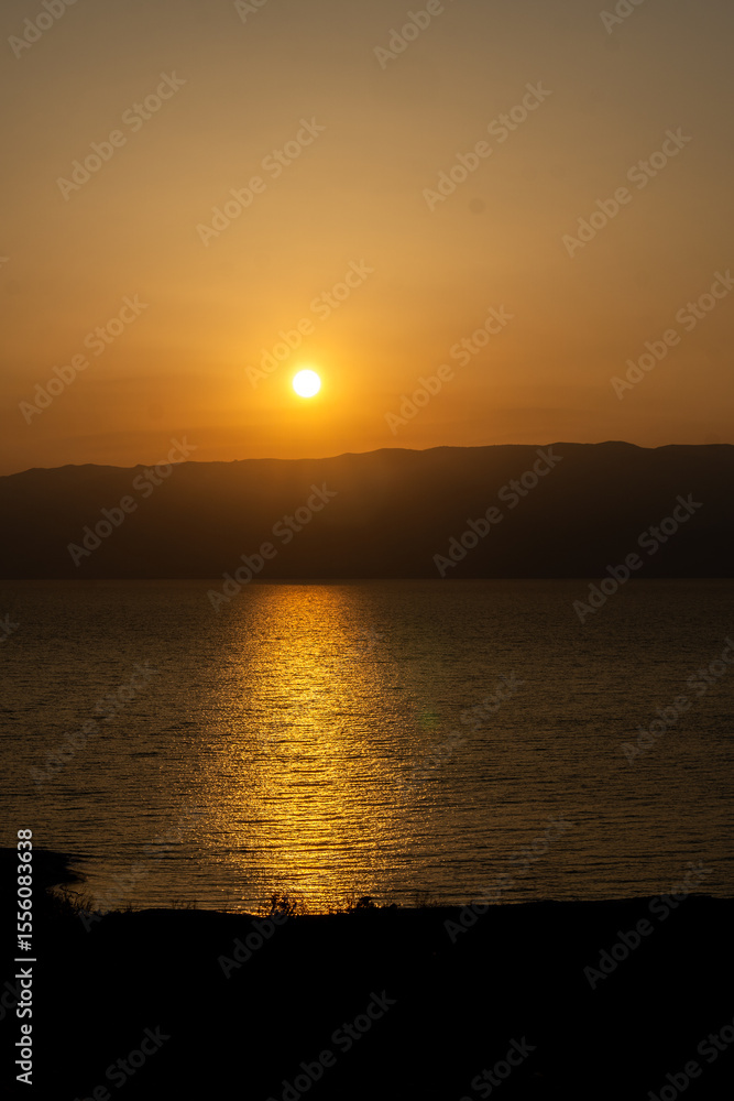 Obraz premium Golden Sunset over the Dead Sea with Mountain Silhouette and Water Reflection