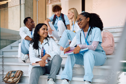 Obraz na płótnie Happy female medical students talking while relaxing on staircase at university