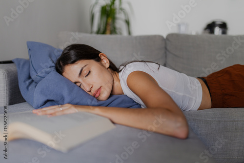 Exhausted young woman sleeping peacefully on a cozy sofa, enjoying a moment of tranquility after immersing herself in a captivating book