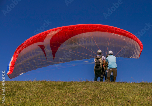 Bild auf Leinwand Preparación para vuelo en parapente biplaza sobre colina con cielo despejado
