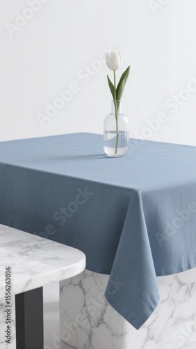Blue tablecloth on a marble table with a single white tulip in a glass vase