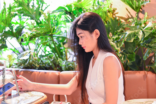 Asian Woman Using Smartphone in a Modern Café Surrounded by Plants