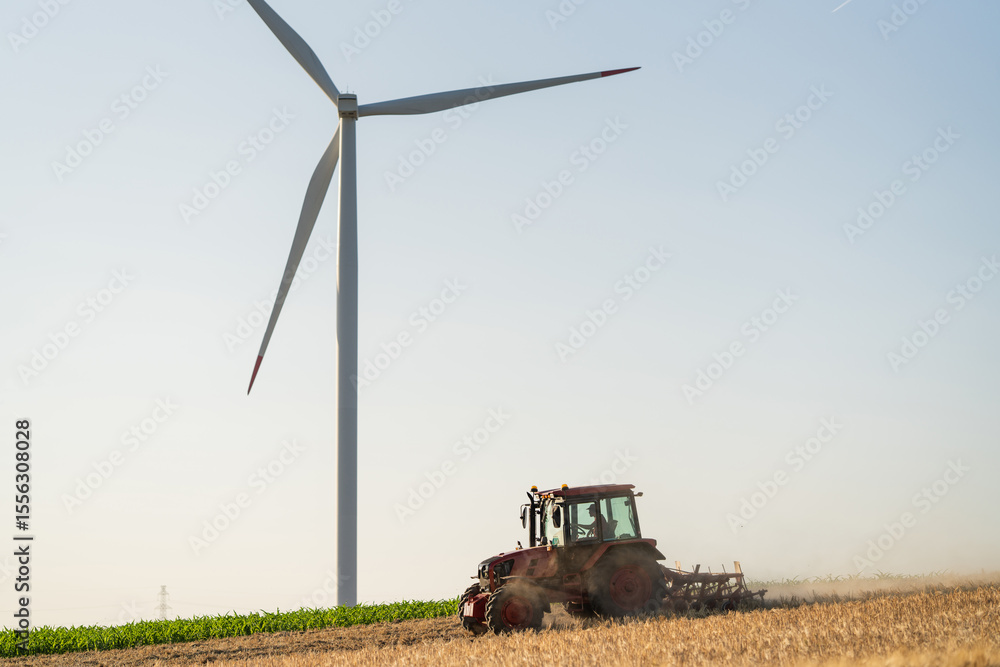 Obraz premium Agricultural tractor is working on the field with wind turbines