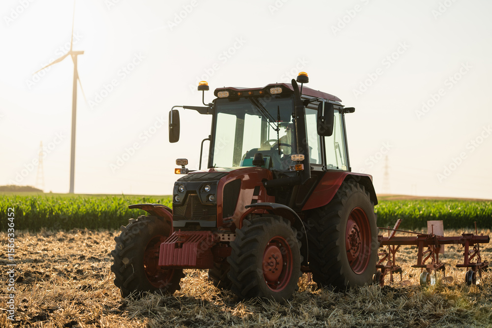 Obraz premium Agricultural tractor is working on the field with wind turbines