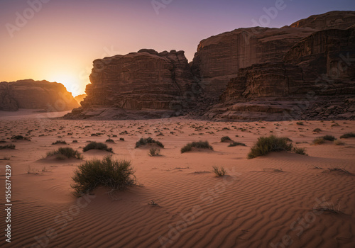 Desert landscape at sunrise with rock formations and cacti in the foreground, warm orange hues dominate the sky
