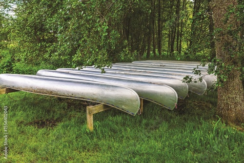 Bilde på lerret Several metal canoes resting upside down on wooden racks in shaded area near forest, ready for summer activities