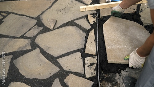 Obraz na plátně Construction worker carefully placing irregular flagstone on a bed of dark morta
