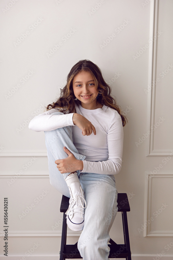 A portrait of a fashionable teenage girl in white clothes and sneakers dancing in a studio on a light wall in a room. light from the window A portrait of a fashionable teenage girl in white clothes and sneakers dancing in a studio on a light wall in a room. light from the window