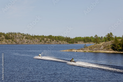 Εκτύπωση καμβά Two people ride jet skis across a clear blue lake surrounded by rocky forested shores on a sunny summer day