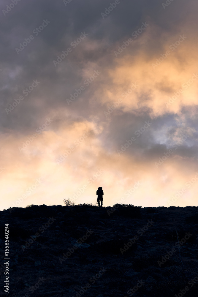 Fototapeta premium Hiker standing on a mountain ridge at dusk in the Alps with dramatic cloud formations