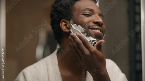 African American man shaving beard applying foamy gel in bathroom bearded guy smear foam shave procedure looking at mirror unshaven bristle male touching skin prepare face care hygiene cosmetic beauty