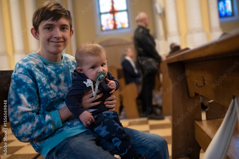 Fotografie Catholic teenage boy with his baby brother on a bench in a church