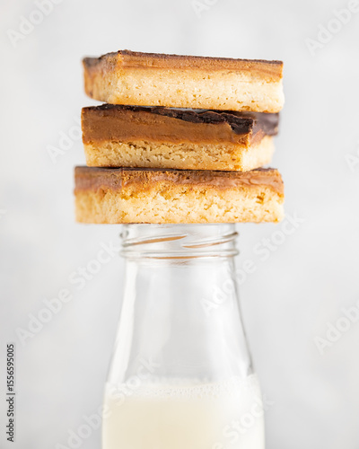 Caramel chocolate shortbread cookie squares stacked on a bottle of milk