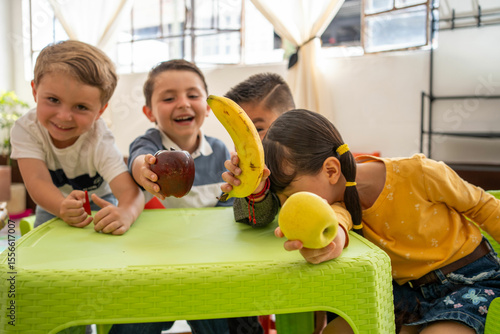 Kindergarten children proudly display fruits during a classroom preschool activity. Focus on healthy eating, nutrition education, and promoting good habits in a diverse learning environment.