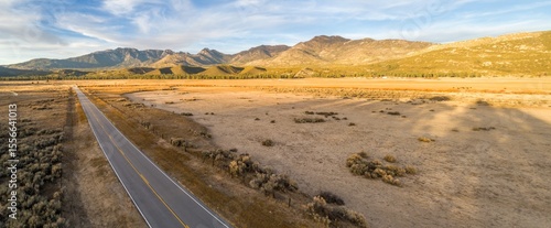 A rural road cuts through a vast, dry landscape in Thomas Mountain, Mountain Center, California, USA, leading towards distant mountains under a clear sky.