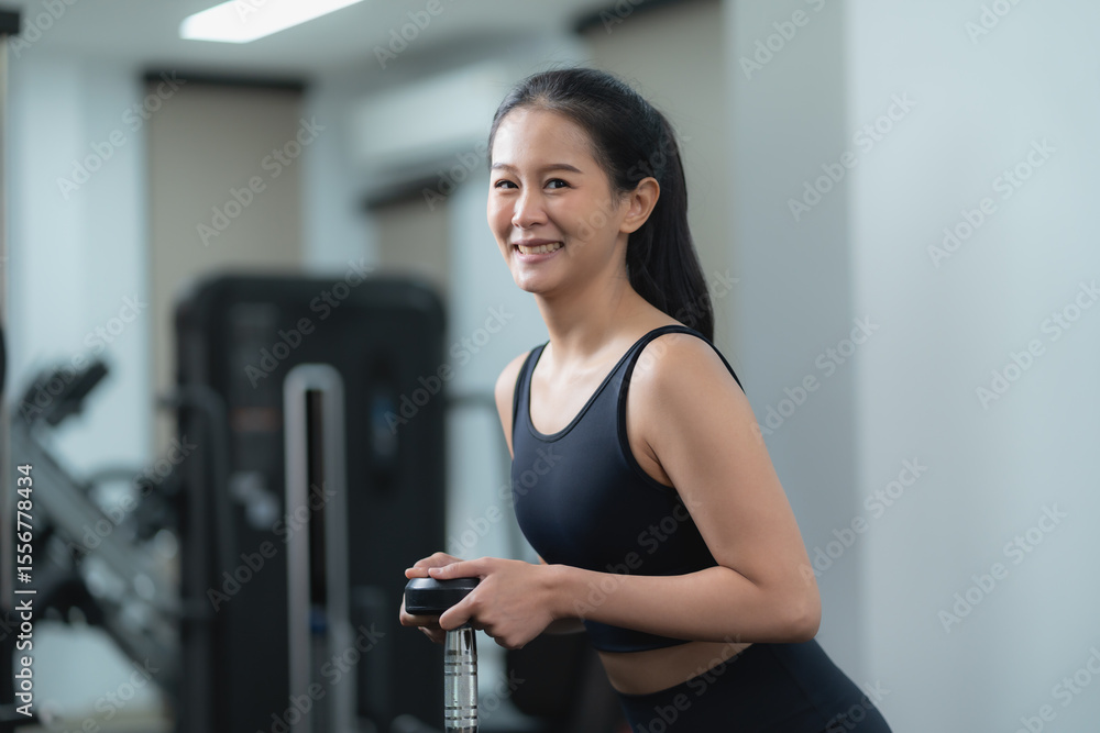 Obraz premium Young asian woman in gym holding dumbbell and performing squat exercise for strength training, focused on fitness, healthy lifestyle, muscle building workout