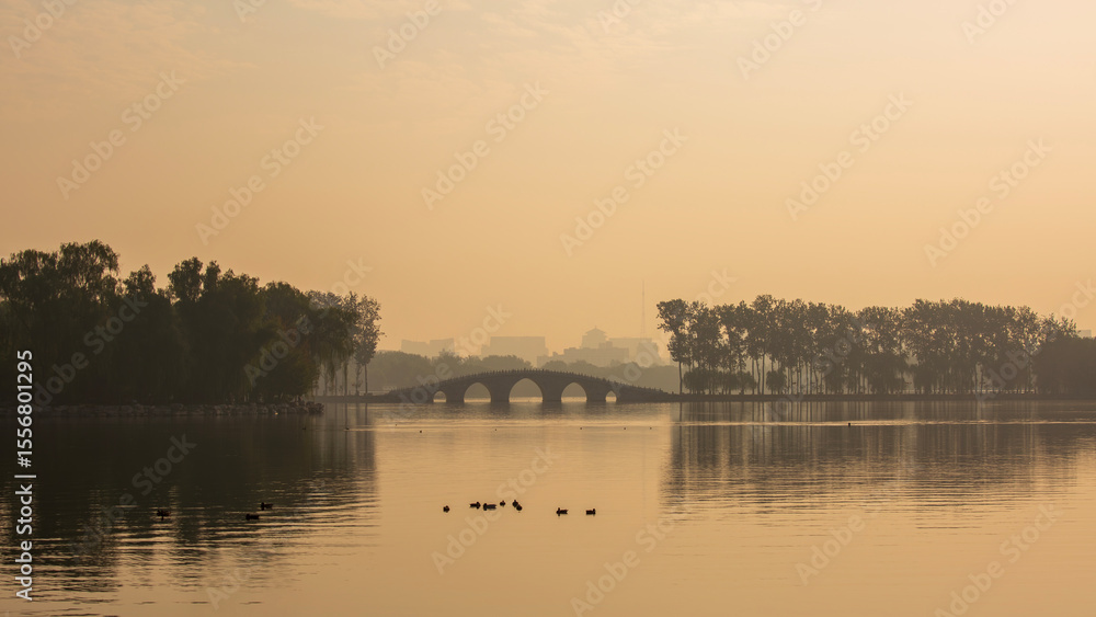 Obraz premium The lake and arched bridge of Beijing's Yuyuantan Park shrouded in morning mist.