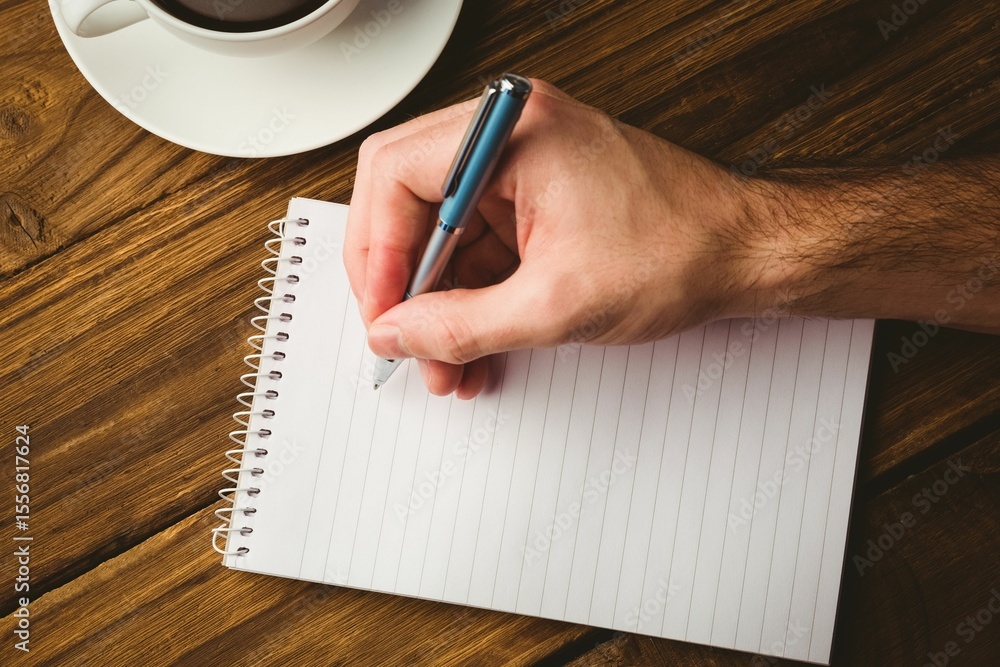 Fototapeta premium Man writing in book by coffee cup on table