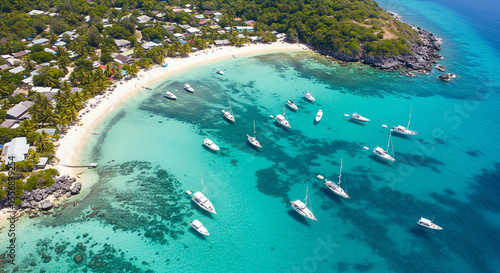 Scenic drone view of yachts and boats anchored in a shallow blue lagoon near a tropical island. Perfect for marine tourism, ocean leisure, and summer escape visuals.