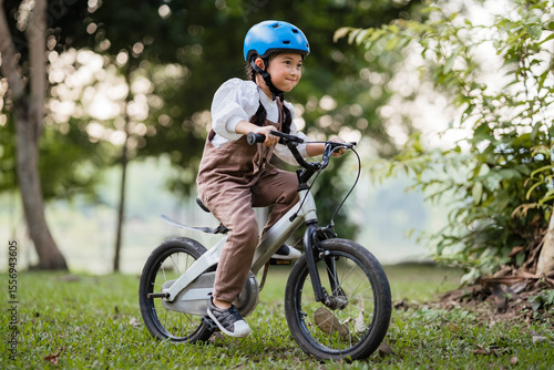 A young boy is riding a bicycle in a park. He is wearing a helmet and a white shirt