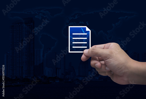 Fototapeta Naklejka Na Ścianę i Meble -  Hand holding document flat icon in fingers over world map, modern city tower and skyscraper, Technology internet online concept, Elements of this image furnished by NASA