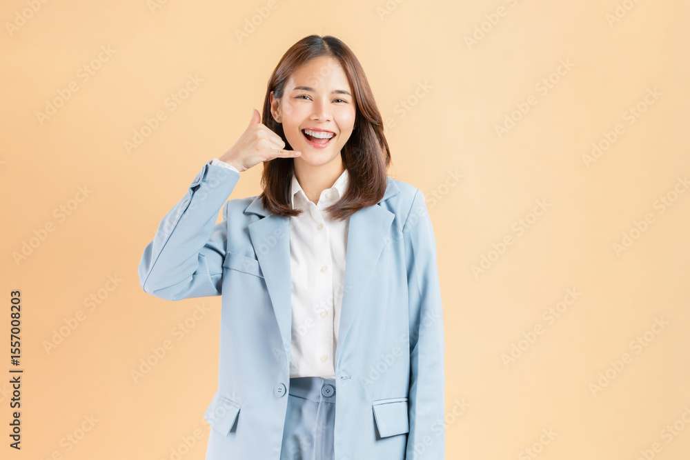 Cheerful Asian businesswoman makes a call me gesture against a beige background. Cheerful Asian businesswoman makes a call me gesture against a beige background.