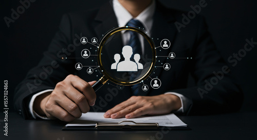 Businessman in Dark Suit Analyzing Candidate Profiles with Magnifying Glass for Recruitment on Table with Clipboard and Document in Indoor Setting