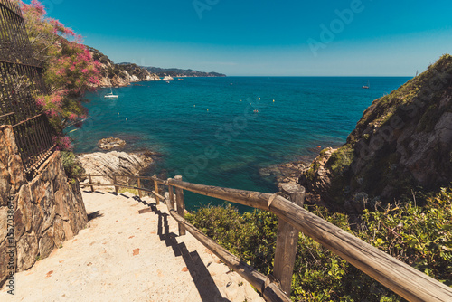Seascape in Blanes, Spain with a sailboat in the background and the cliff promenade called Cami de Ronda in the foreground. Costa Brava.