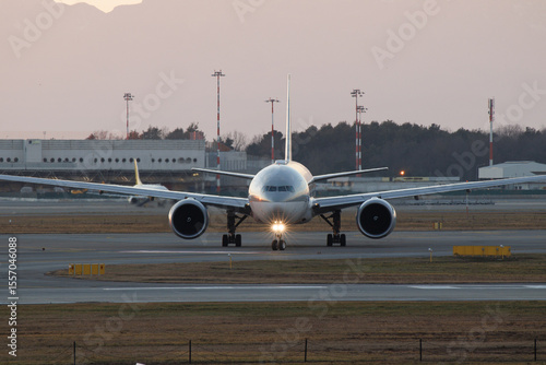 Front view of commercial airplane taxiing on airport runway at dusk
