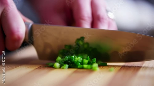 Close-up of hands expertly chopping fresh green herbs with a knife on a wooden cutting board, preparing ingredients for cooking.