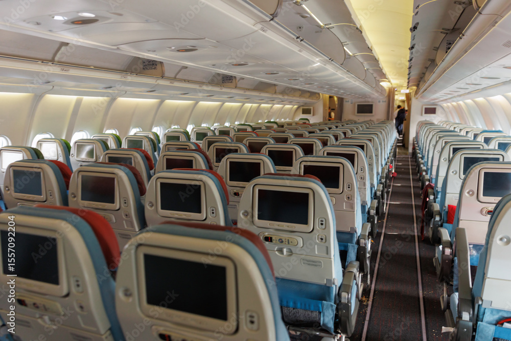 Obraz premium Rows of empty seats are visible within the airplane cabin, highlighting the airline's seating arrangement and onboard amenities. Soft lighting and a narrow aisle create a calm atmosphere.