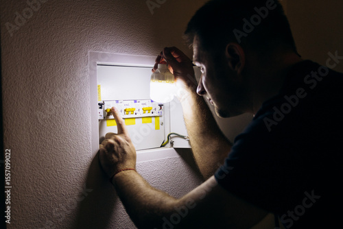 Power outage. A man holds an LED lamp in front of an electrical panel.