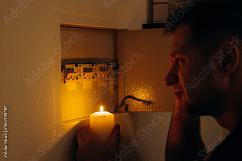 Power outage. A man holds a candle in front of an electrical panel.