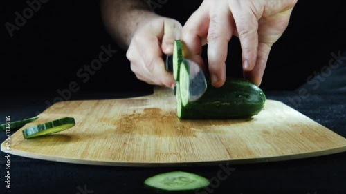 Close-up of hands slicing a cucumber on a wooden cutting board.