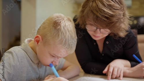 A mother patiently helps her son with a hearing aid complete homework together. Authentic moment of bonding, education and rehabilitation. Perfect for inclusive parenting and special needs content