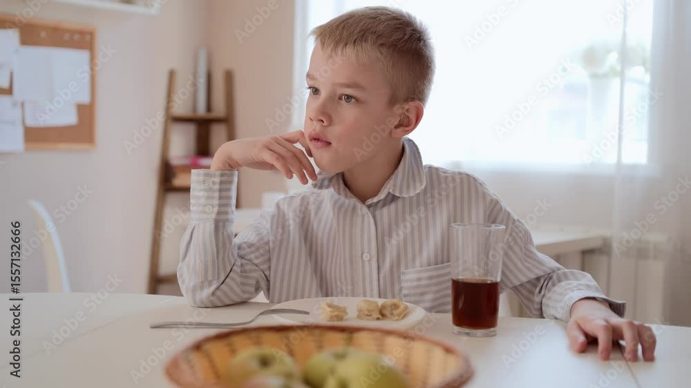 A young boy with a hearing aid enjoys his breakfast at the kitchen table. Natural morning light, cozy atmosphere, and authentic child emotions. Perfect for family, health, and lifestyle content A young boy with a hearing aid enjoys his breakfast at the kitchen table. Natural morning light, cozy atmosphere, and authentic child emotions. Perfect for family, health, and lifestyle content
