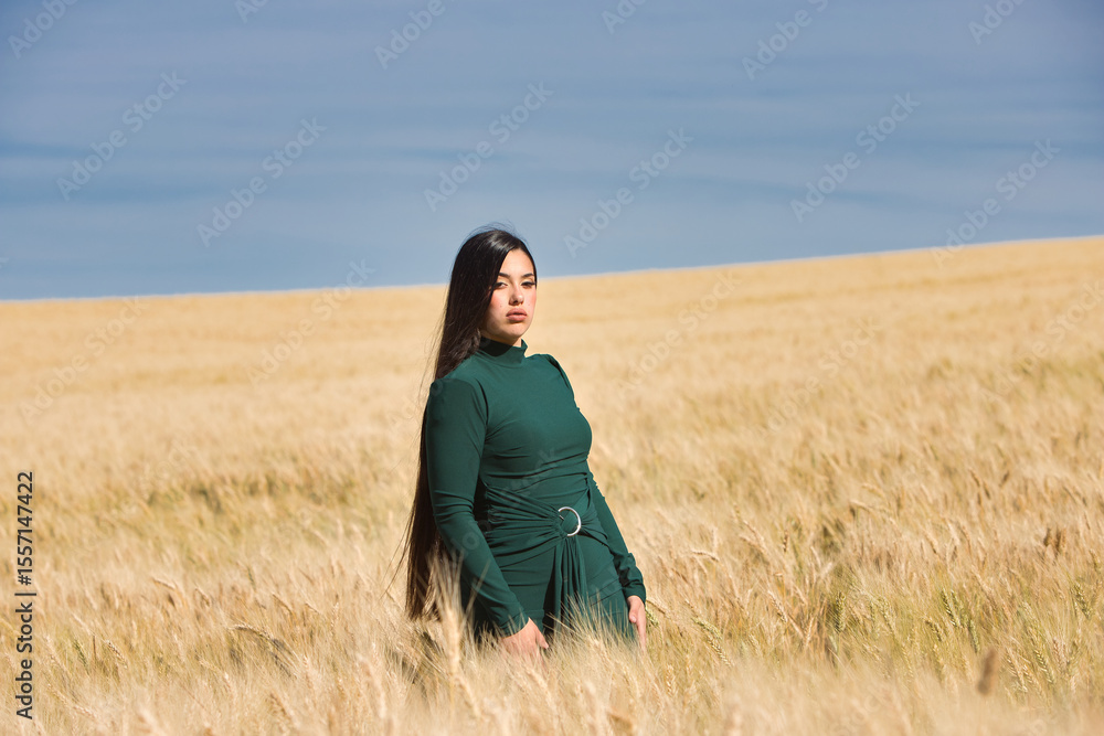 A beautiful, dark-haired teenage Latin girl dressed in green stands among a dry, yellow wheat field on a summer day. In the background, the blue sky. A beautiful, dark-haired teenage Latin girl dressed in green stands among a dry, yellow wheat field on a summer day. In the background, the blue sky.