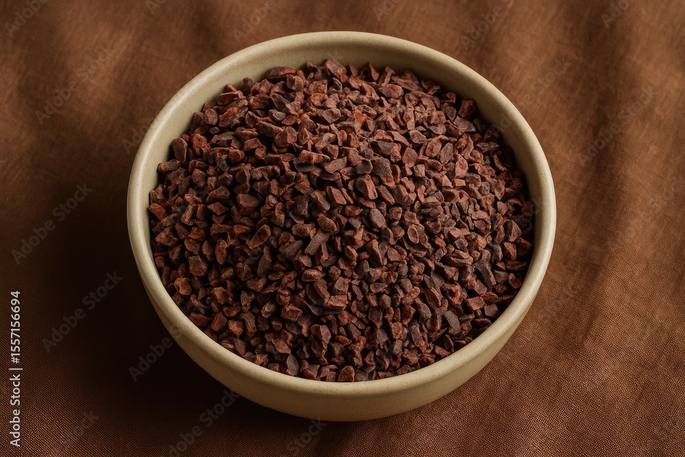 Chocolate nibs in a bowl placed on a rustic fabric surface Chocolate nibs in a bowl placed on a rustic fabric surface