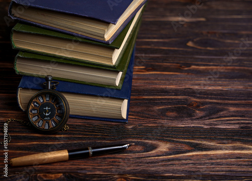Stack of books with vintage pocket watch and fountain pen on wooden table